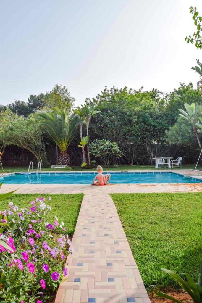 Mother and daughter sits around a Moroccan pool at Moroccan accommodation, surrounded by lush gardens.