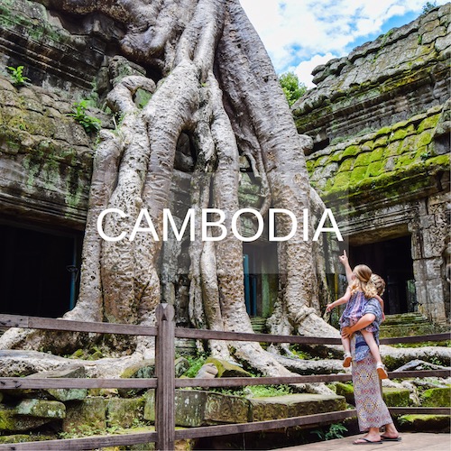 Mother and child stand in Ta Prohm temple, looking up at the enormous trees.