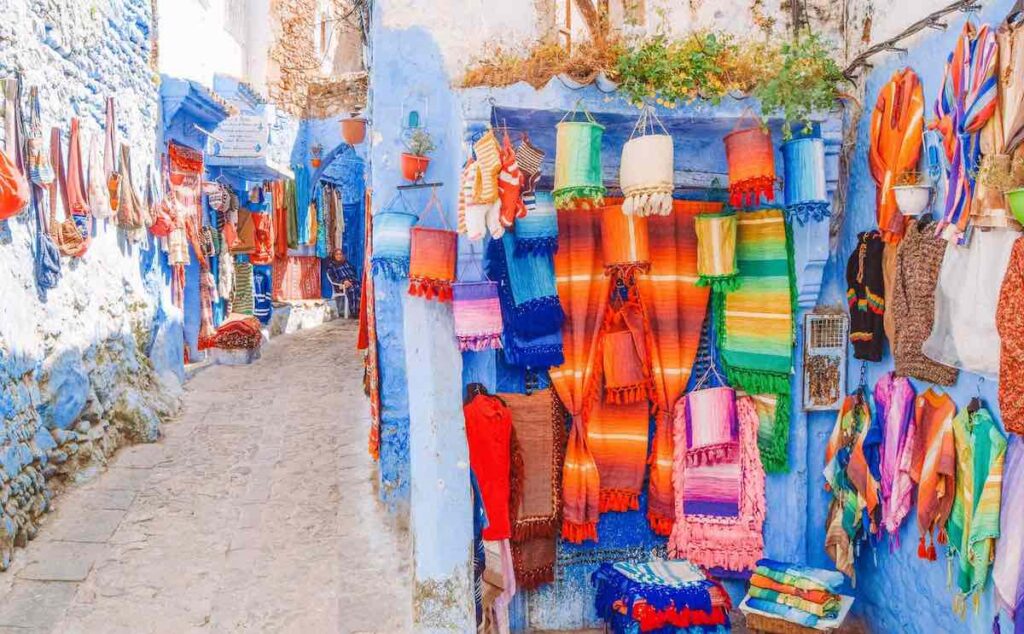 Brightly coloured rugs hang off Chefchaouens blue street wall