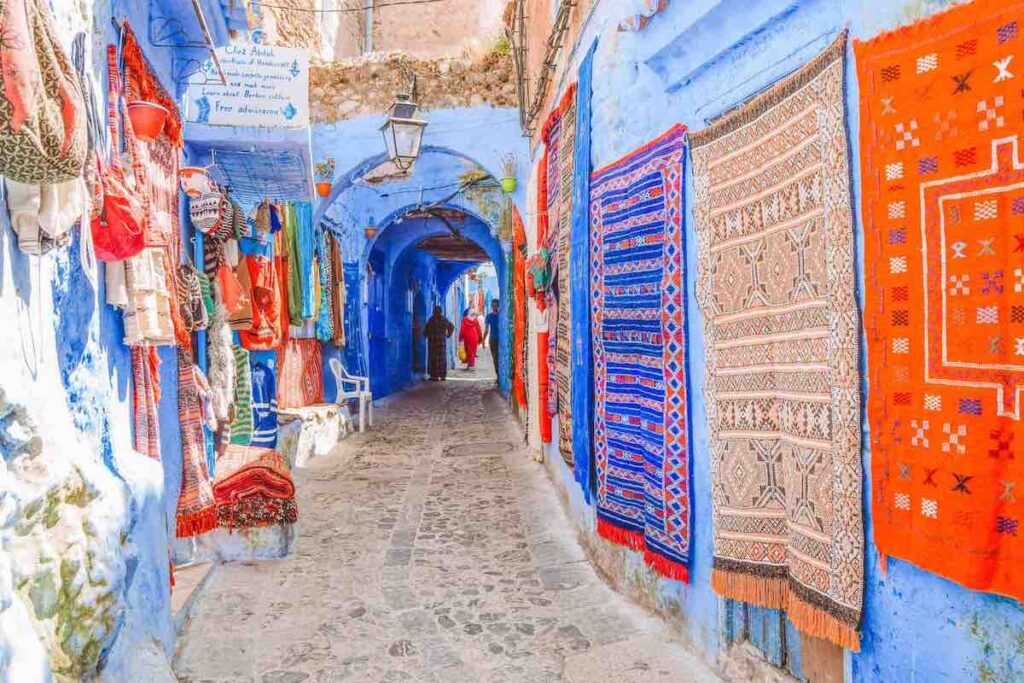 Bright blue street in Chefchaouen with colourful carpets hanging on the walls