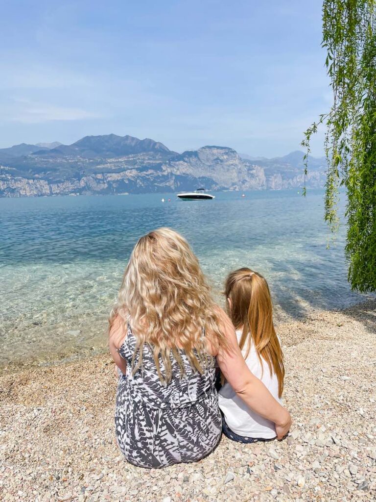 Mother and daughter sit on the edge of Lake Garda