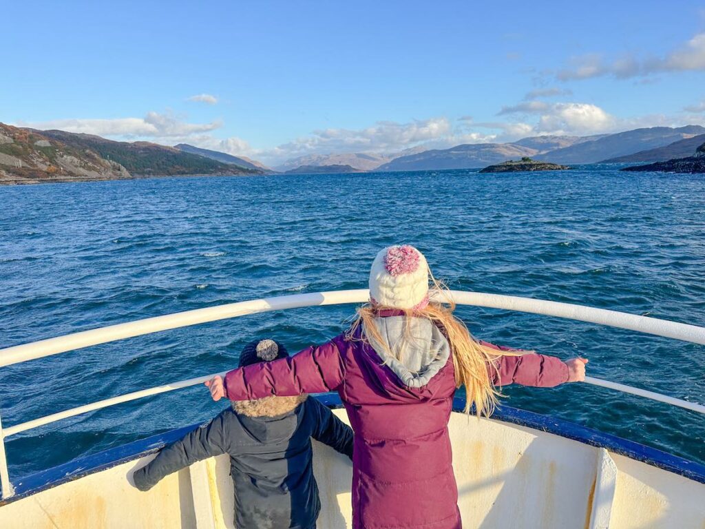 Children stand on the front of a boat going across a Scottish Loch