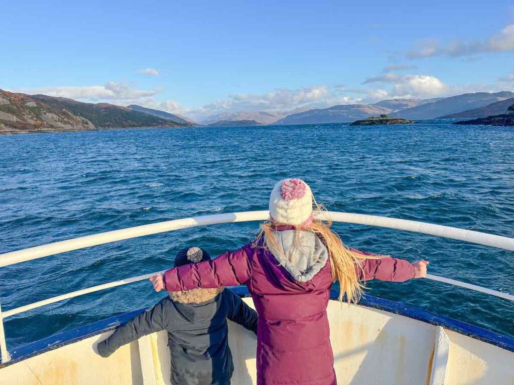 Two children stand on a boat looking out over Loch Ness