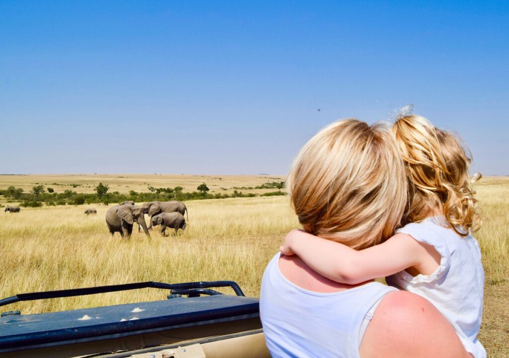 Young girl with her mother in a safari jeep, watch a herd of Elephants, which are grazing nearby