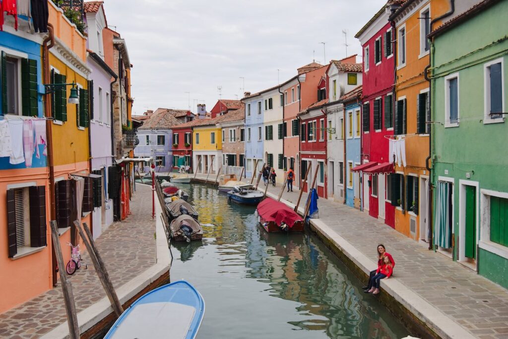 Mother and daughter sitting by a canal on Burano with colorful houses