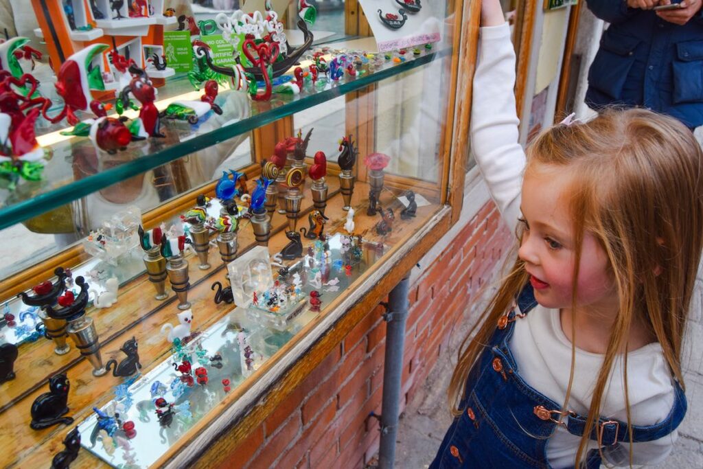 Child looking into a Murano glass shop window, admiring colorful blown glass ornaments on Murano Island, Venice