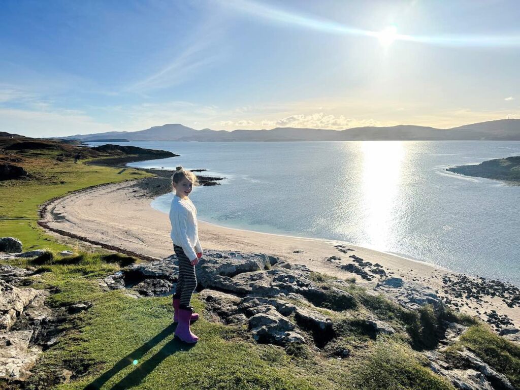Child standing on a viewpoint overlooking the turquoise waters and sandy Coral Beach on the Isle of Skye.