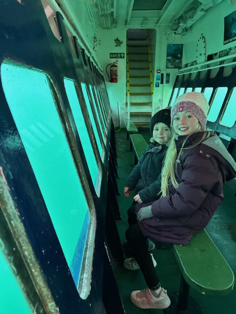 Children enjoying the SeaProbe Atlantis glass-bottom boat near the Isle of Skye, Scotland, looking at marine life below.