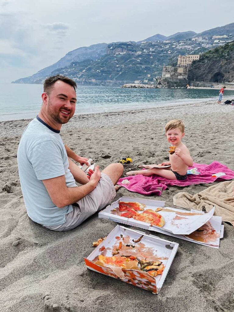 Father and son eating pizza together on Maiori Beach on the Amalfi Coast.