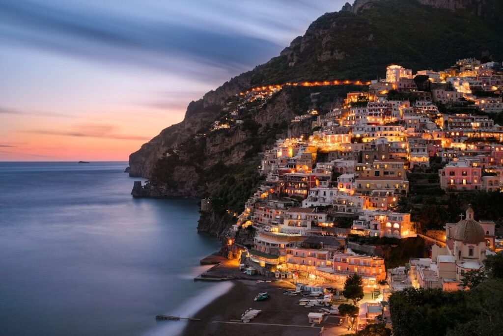 Night-time view of the Amalfi Coast in Italy with illuminated coastal towns and sea.

Description: